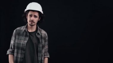 Mühendisin beyaz miğferli karizmatik çocuğu sağ tarafı işaret ediyor, hayır diyor ve hoşlanmadığını gösteriyor. Siyah arka planda izole edilmiş. Hayat kavramı. İnsanların duyguları işte. 4k portre