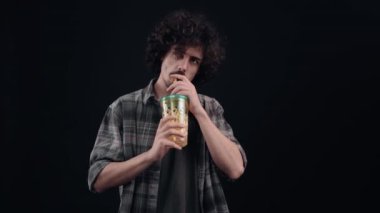 Yakışıklı, yakışıklı ve susamış çocuk pipetle bardaktan içer, harika tadı karşısında hayrete düşer, bardağı gösterir ve benzer bir işaret gösterir. Siyah arka planda izole edilmiş. Konsept: