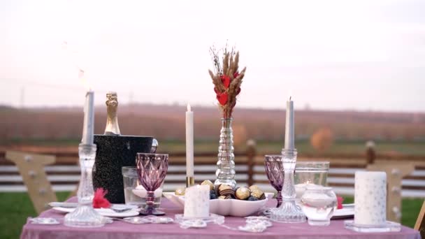 Het romantische decor van een tafel ingericht in het midden van de natuur met kaarsen, bestek, champagne en bomobaan. 4k portret — Stockvideo