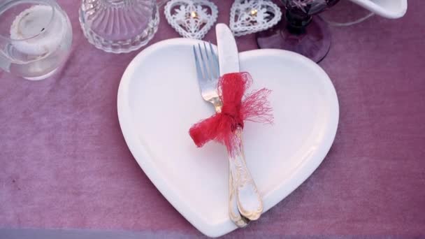 Marco cerrado de la placa en forma de corazón en el que están cubiertos atados con un hermoso encaje rojo. Pequeño detalle en la mesa donde tiene lugar la cena romántica. Retrato 4k — Vídeos de Stock