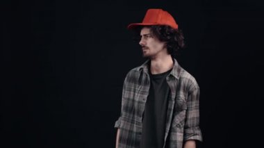 Kırmızı şapkalı tiksinmiş genç adam mesafeyi koruduğunun bir göstergesi olarak ellerini bir tarafa kaldırmış gibi görünüyor. Siyah arka planda izole edilmiş. Hayat kavramı. İnsanların duyguları işte. 4k portre