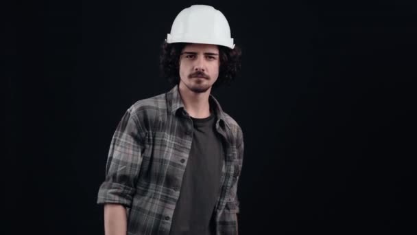 Portrét charismatického inženýra s bílou helmou upevňující rám rukama. Izolované na černém pozadí. Pojem "život". Lidské emoce. 4k portrét — Stock video