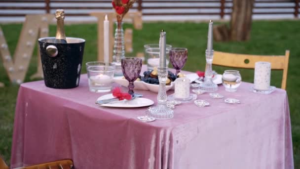 Ρομαντικό γεύμα έτοιμο για έρωτα, ρομαντικό σκηνικό στο πράσινο γρασίδι, τραπέζι διακοσμημένο με κεριά, ποτήρια, μαχαιροπίρουνα, σοκολάτες και ένα μπολ γεμάτο σοκολάτες και μούρα. 4k πορτρέτο — Αρχείο Βίντεο