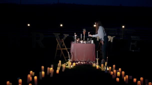 Cadre distant d'une fille allumant des bougies et les arrangeant sur la table romantique. Cadre de nuit de la table décorée pour le couple, entouré de bougies, et sur le dos les lettres sous la forme de — Video