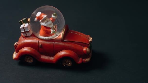 Cadre en gros plan, filmé d'un côté, de petit jouet, voiture rétro rouge avec le Père Noël au volant et cadeaux dans le coffre. Jouets pour enfants, concept d'hiver. Noël et Nouvel An — Video