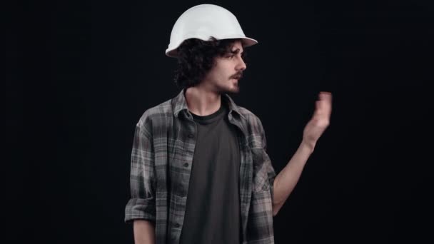 Інженер з білим шоломом вказує індексним пальцем на одну сторону і показує подібний знак. Ізольовані на чорному тлі. Поняття життя. Люди емоції. портрет 4k — стокове відео