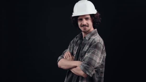 The proud engineer, in a white helmet, stands straight with an arrogant look and looks ahead with his hands folded across his chest. Isolated on black background. The concept of life. Peoples — Stock Video