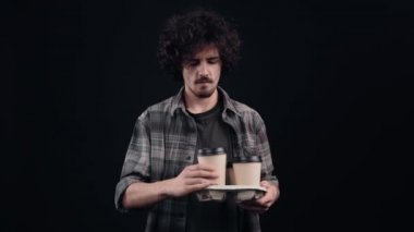 Genç hippi tezgahtan dört kahveyle bir bardak alır, susuzluktan içer ve keyifle başını sallar. Siyah arka planda izole edilmiş. Hayat kavramı. İnsanların duyguları işte. 4k portre