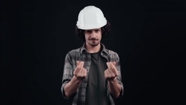 Mazaný inženýr s bílou helmou si tře prsty, aby naznačil, že mu musí být zaplaceno. Izolované na černém pozadí. Pojem "život". Lidské emoce. 4k portrét — Stock video