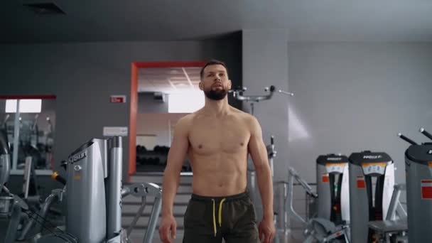 El hombre musculoso confiado, con el pecho desnudo, camina orgullosamente hacia adelante en el gimnasio. Entrenamiento intensivo. Intensa energía masculina. Estilo de vida saludable. Concepto deportivo — Vídeos de Stock