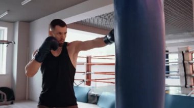 Yakışıklı adam spor salonundaki boks ringinde kum torbasıyla antrenman yapıyor. Yoğun erkeksi enerji. Sağlıklı bir yaşam tarzı. Spor konsepti