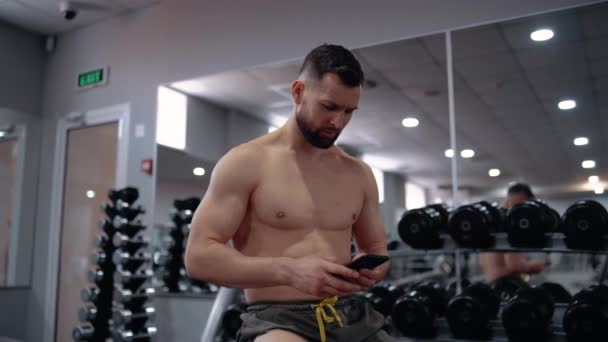 De serieuze bodybuilder zet de volgende nummers op de telefoon te spelen tijdens de training. Intense mannelijke energie. Een gezonde levensstijl. Sport concept — Stockvideo