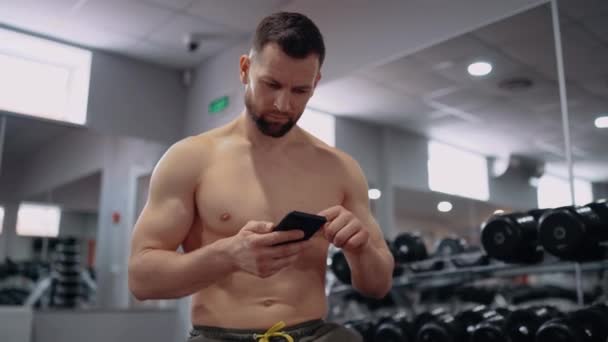 El atleta serio y cansado navega por Internet en el gimnasio. Intensa energía masculina. Estilo de vida saludable. Concepto deportivo — Vídeo de stock