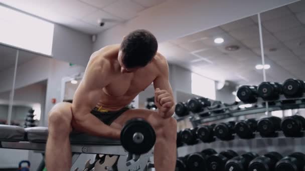 Den unga tränaren visar hur man lyfter hanteln korrekt med ena handen i gymmet. Intensiv maskulin energi. En hälsosam livsstil. Idrottsbegreppet — Stockvideo