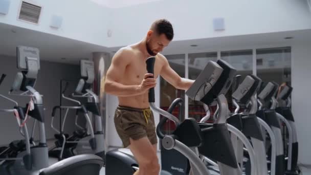 De jonge sporter traint op de elliptische fiets in de sportschool. Intense mannelijke energie. Een gezonde levensstijl. Sport concept — Stockvideo