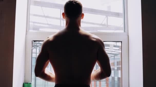 Die muskulösen Männer lehnen sich an ein Fenster, der Mann schaut aus dem Fenster, der hintere Rahmen. Intensive männliche Energie. Gesunder Lebensstil. Sportkonzept — Stockvideo