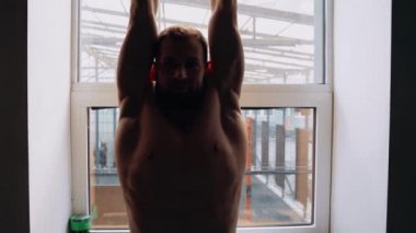 Camdaki kaslı adam ellerini yukarı doğru uzatıyor ve sonra pazılarını ve göğüs kaslarını geriyor. Yoğun erkeksi enerji. Sağlıklı bir yaşam tarzı. Spor konsepti