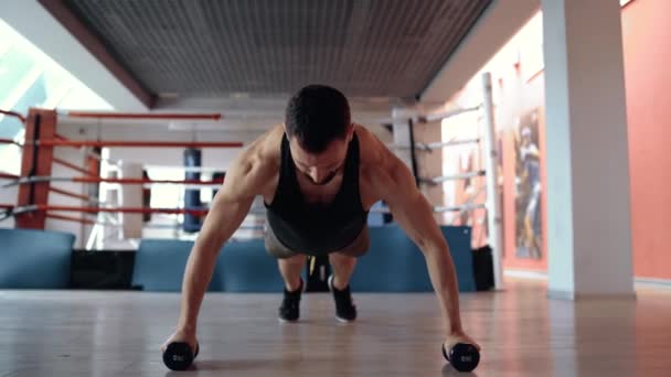 Ein trainierter, motivierter Mann macht Liegestütze mit den Händen an Hanteln in einem Fitnessstudio. Gesunder Lebensstil. Sportkonzept — Stockvideo