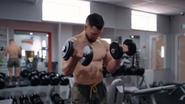 Çekici, sportif adam halterleri kaldırarak pazı egzersizleri yapıyor. Yoğun erkeksi enerji. Sağlıklı bir yaşam tarzı. Spor konsepti