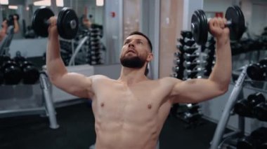 Spor salonunda kafasının üstüne dambıl kaldıran kaslı bir gencin portresi. Yoğun erkeksi enerji. Sağlıklı bir yaşam tarzı. Spor konsepti