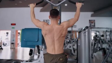 The handsome, bare-backed bodybuilder pumps his back muscles into the gym. Intense masculine energy. Healthy lifestyle. Sport concept