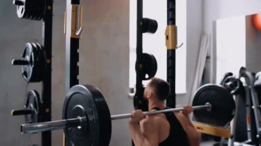 Vücut geliştiricinin arkasındaki manzara, halterle boynunda ağırlık olan çömelmeler sergiliyor. Yoğun eğitim. Yoğun erkeksi enerji. Sağlıklı bir yaşam tarzı. Spor konsepti