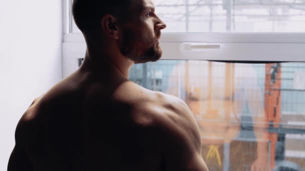 Primer plano de un joven musculoso con el pecho desnudo mirando por la ventana. Intensa energía masculina. Estilo de vida saludable. Concepto deportivo — Vídeos de Stock