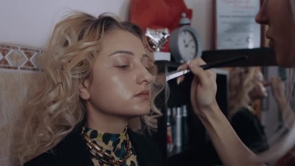 The young make-up artist applies a foundation brush on the face of the woman with blonde hair. The process of applying makeup at home. Artistic concept — Stock Video