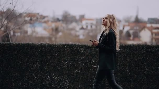 The charismatic young woman walks, in profile, with a serious face with the phone in her hand dressed in a jacket, with a shrill make-up. Female energy. Beauty industry. Artistic concept — Stock Video