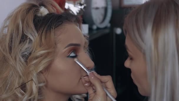 De jonge make-up artiest accentueert de blauwe lijn onder de ogen met het aanbrengen van een concealer. Het proces van het aanbrengen van make-up thuis door een professional. Artistiek concept — Stockvideo