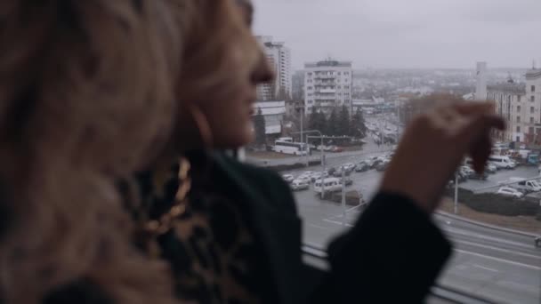 De blonde met krullend haar speelt met haar vingers op het raam wat een prachtig uitzicht over de stad onthult. Vrouwelijke energie. Schoonheidsindustrie. Artistiek concept — Stockvideo
