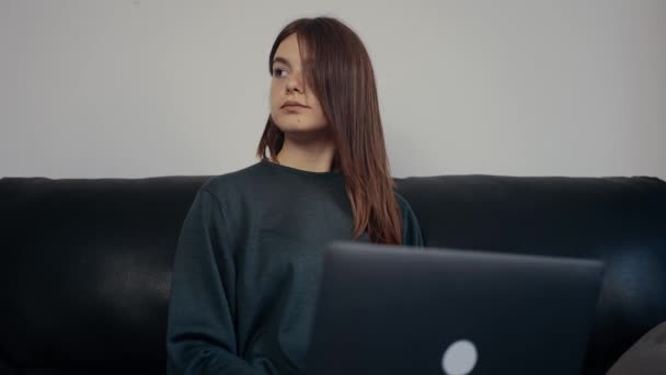 Das Mädchen mit roten Haaren und Sommersprossen arbeitet konzentriert an einem College-Projekt, studiert intensiv, reflektiert einige Konzepte, sitzt auf einem schwarzen Sofa. 4k-Konzept — Stockvideo