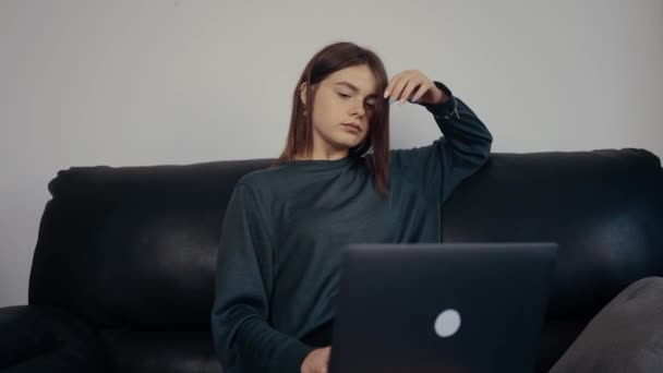 Bizneswoman pracuje nad projektem, zostawia ją, układa włosy, a następnie kontynuuje pisanie nowych pomysłów na laptopie. Ubrany w ciemnozieloną walizkę, siedzący na czarnej sofie. 4k — Wideo stockowe