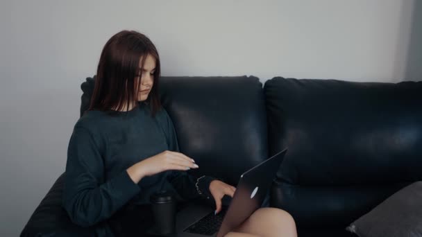 비지니스 여성은 온라인으로 소파에 앉아 일하고, 사려깊게 보이고, 사업에 집중 합니다. 짙은 녹색 가방을 걸치고 검은 소파에 앉아 있었다. 작업 개념. 4k 개념 — 비디오