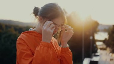 Gözlüklerini takan kızıl saçlı bir öğrencinin portresi kameraya bakar ve gülümser. Peri masalı günbatımının arka planında, parkın girişine yerleştirilmiş turuncu bir bluz giymişti.