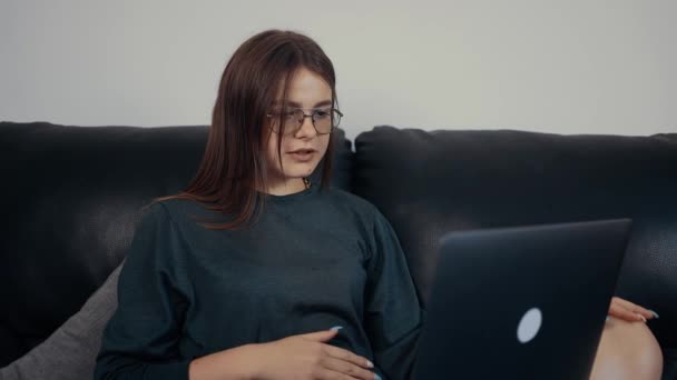 A jovem mulher inspirada, vermelha com sardas e óculos, ensina uma lição muito importante on-line para seus alunos. Vestida com uma blusa verde escura, sentada em um sofá preto. O conceito de trabalho — Vídeo de Stock