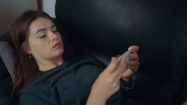 Genç kızıl saçlı, kanepede uzanmış, telefonda video oyunları oynarken yakın plan çekimler. Çağdaş kadın kavramı. 4k konsepti