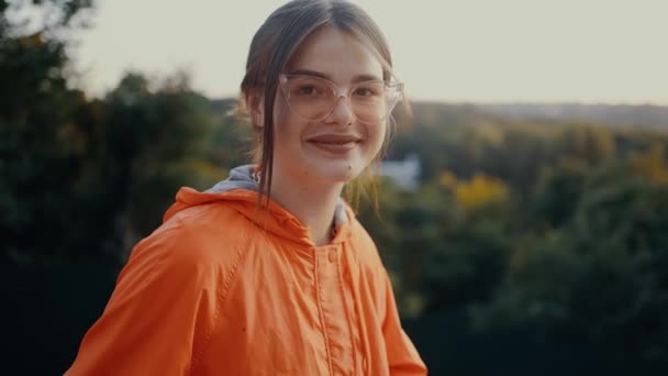 Het portret van een optimistische jonge vrouw, in de natuur met een brede glimlach. Gekleed in een oranje blouse, haar gevangen in een broodje, draagt ze een bril. 4k-concept — Stockvideo