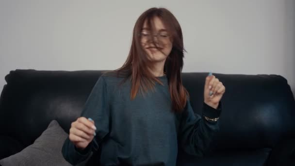 El estudiante pelirrojo y feliz con gafas baila felizmente después de pasar con éxito todos los exámenes. Pelirroja, vestida con una blusa verde oscuro. El concepto de la mujer relajándose en casa. Concepto 4k — Vídeos de Stock