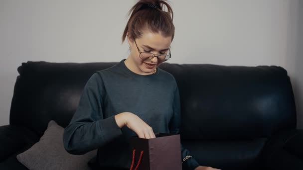 The young redhead, with glasses, opens the gift and is surprised by what she receives. Take the pictures out of the box and look at the paintings with nostalgia. Dressed in a dark green blouse — Stok Video
