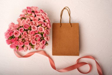 Kalp şeklinde bir buket pembe gül ve hafif arka planda bir el çantasındaki hediye.