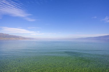 Yeşil ağaçların, dağların, turkuaz suların ve güneşin doğuşunda mavi gökyüzünün inanılmaz manzarası. Deniz kıyısındaki dağlarda yaz manzarası.