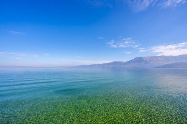Yeşil ağaçların, dağların, turkuaz suların ve güneşin doğuşunda mavi gökyüzünün inanılmaz manzarası. Deniz kıyısındaki dağlarda yaz manzarası.