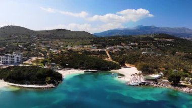 Güneşli bir günde İyon Denizi 'nde güneşsiz güneşli bir sahilin havadan görünüşü. Kamera yavaşça döner. Ksamil, Arnavutluk.