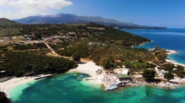 Güneşli bir günde İyon Denizi 'nde güneşsiz güneşli bir sahilin havadan görünüşü. Kamera yavaşça döner. Ksamil, Arnavutluk.