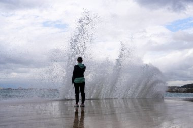 Büyük fırtınalı dalgalar şehir seti yakınlarında çarpışıyor, arka planda dramatik bir gökyüzü. Büyük deniz dalgası sıçraması. Fırtınalı havada dev dalgalar. Vatandaşlar gezinti güvertesinde