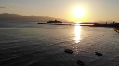 Büyük bir yolcu gemisinin silueti ve altın gün batımlı bir sürü balıkçı teknesi.