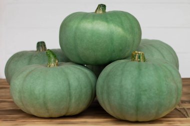 Beyaz arka planda, ahşap masanın üstünde duran yeşil balkabakları.