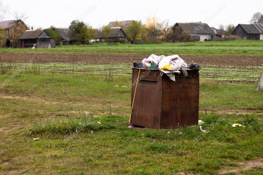 Overflowing rusty trash can in the countryside. Rubbish scattered on the ground. Environmental protection problem