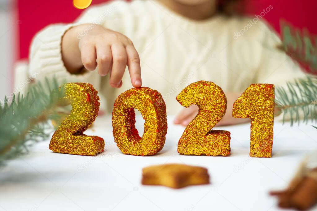 Children's hand touches golden shiny numbers 2021, Merry Christmas and Happy New Year.